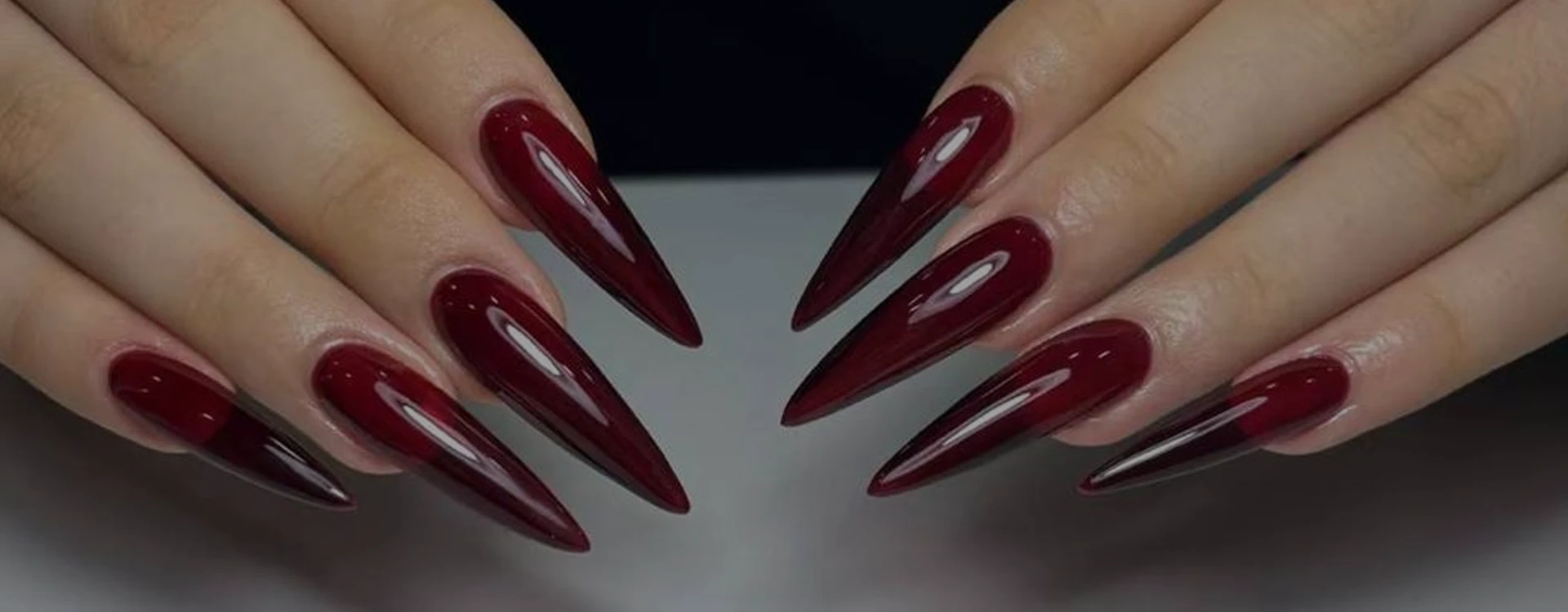 Deep red glossy stiletto acrylic nail set created by a Nail Box student